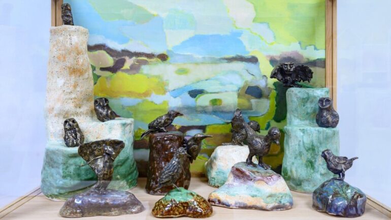 Colour photograph of a sculpture. The sculpture is made from small bronze birds.